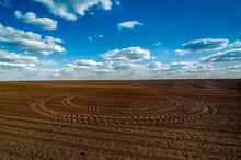 Plowed Field Prepared For Sowing And Tracks Of Tractor Tires, Beautiful Blue Sky With Clouds