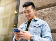 © Jose Carlos Cerdeno/ADDICTIVE STOCK - Content young Asian male in casual outfit browsing on mobile phone while standing near stone wall of urban building