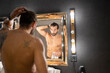 © Jose Carlos Cerdeno/ADDICTIVE STOCK - Shirtless tattooed male looking at mirror and doing ponytail in illuminated contemporary bathroom