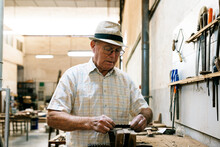 Senior Male Carpenter Grinding Wooden Details While Making Handmade Folding Fans In Messy Workshop