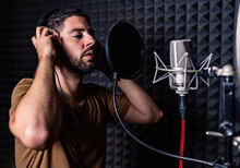 Side View Of Male Singer In Headphones Standing In Acoustic Room With Soundproof Walls And Microphone And Recording Song In Studio