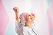 © Jose Luis CARRASCOSA/ADDICTIVE STOCK - Determined mature woman in pink head cover and belt fighting karate in cancer battle concept doing victory gesture in the street on pink wall looking up