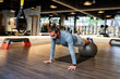 © Jose Carlos Cerdeno/ADDICTIVE STOCK - Bearded adult male athlete holding legs on fit ball and doing abdominal crunches on mat during fitness training in gym