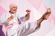 © Jose Luis CARRASCOSA/ADDICTIVE STOCK - Determined cheerful mature barefooted woman in pink head cover and belt kicking fighting karate in cancer battle concept in the street on pink wall looking away
