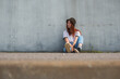 © Nacho Zaitsev/ADDICTIVE STOCK - Full body of trendy teen red haired female student in casual outfit and hat leaning back on gray shabby concrete wall on urban street
