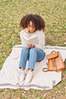 © PHILIPPE DEGOOTE/ADDICTIVE STOCK - Positive African American curly haired female sitting on blanket in autumn park with interesting book while enjoying weekend