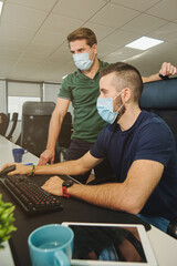 From above of male coworkers in medical masks together using program for software during coronavirus pandemic