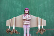 © Sergio Victor Vega/ADDICTIVE STOCK - Cute girl in pilot helmet and handmade creative carton wings standing on street on green background looking up