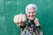 © Sergio Victor Vega/ADDICTIVE STOCK - Cheerful elderly gray haired lady in stylish colorful blouse having fun and boxing at camera while standing against green wall