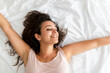 © Sergio Victor Vega/ADDICTIVE STOCK - Top view of delighted female lying on bed and stretching after awakening in bedroom in morning