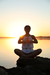 Wall Mural - Woman practicing yoga near river on sunset. Healing concept