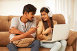 © krishna - Happy young couple using laptop at home on sofa.