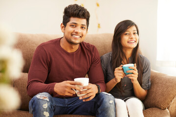 Wall Mural - Cheerful young beautiful couple having coffee together on sofa at home.