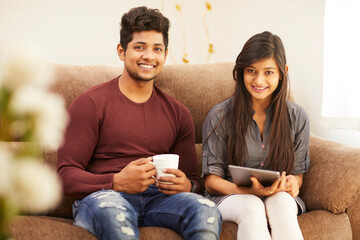 Wall Mural - Cheerful young beautiful couple chatting with tablet and coffee on sofa at home.