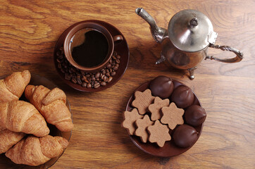 Two cups of coffee, coffee pot, coffee grinder, croissants on a saucer, saucer with cookies and chocolates on wooden texture.