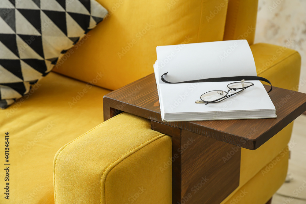 Eyeglasses and book on armrest table in room