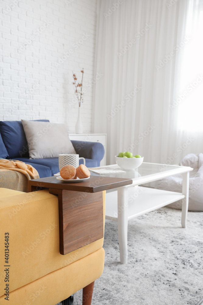 Cup of tea and cupcakes on armrest table in room