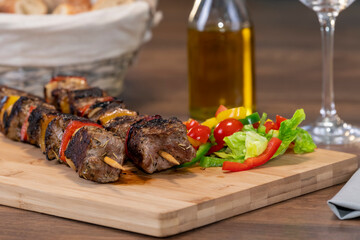 two beef skewers next to assorted cut vegetables on a wooden cutting board