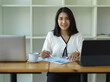 © bongkarn - Businesswoman smiling to camera while reading paperwork in office room