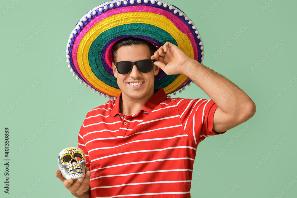 Young man in sombrero hat and with skull on color background. Celebration of Mexico's Day of the Dead