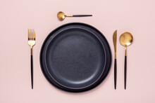 Dark Ceramic Plates And Gold And Black Cutlery On Pastel Pink Background. Top View