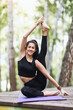 © Sergey Chayko - Satisfied young brunette woman in black sportswear practices yoga, doing Surya Yantrasana exercise, sitting in a compass pose on a wooden bridge in the park