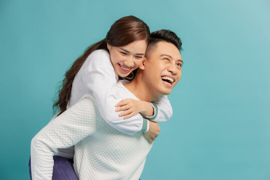 Image of lovely couple having fun while man piggybacking his girlfriend isolated over blue background