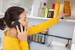 © auremar - woman taking ingredient from cupboard while talking on telephone