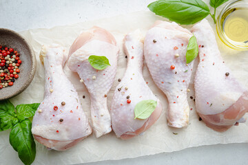 Wall Mural - Raw chicken drumsticks on paper with herbs and seasonings on white background. Top view with copy space for your text.