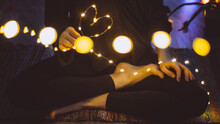 Woman Seated Cross-legged With Bokeh Christmas Lights In A Heart Shape. Concept: Love And Magic In Simplicity	