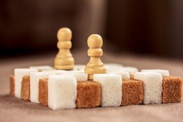 White and brown sugar cubes in form of a chessboard and two chessmen on it.  Closeup. Copy space