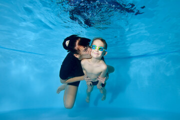 a beautiful boy and his mother swim together under the water. she kisses him gently on the cheek. ac