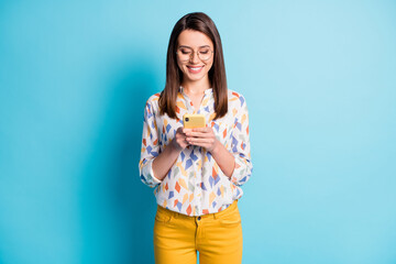 Wall Mural - Photo of cute young girl hold telephone look screen wear specs geometry print shirt yellow pants isolated blue color background