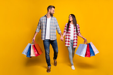 Full length photo portrait of man and woman holding hands going shopping with bags isolated on vivid yellow colored background