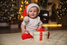 Cute Baby In Santa Hat With Christmas Gift On Floor At Home