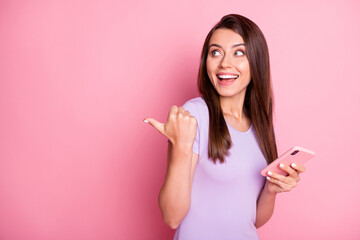 Poster - Photo of funky excited young woman brown hair hold phone show pointing gesture look empty space dressed purple t-shirt isolated on pink color background