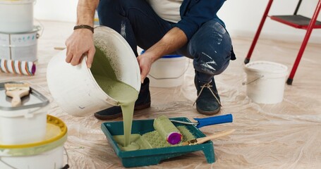 Close up of Caucasian young handsome man pouring green olive paint preparing for painting walls in house renovating and redesigning room. Handyman working on apartment redecoration repair and makeover