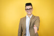 © Irene - Young business man over isolated yellow background smiling friendly offering handshake as greeting and welcoming
