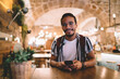 © BullRun - Cheerful ethnic man surfing smartphone and sitting in cafe