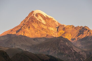 Wall Mural - Beaitiful scenic view of KAzbek mountain top during sunrise and Gergeti church in foreground