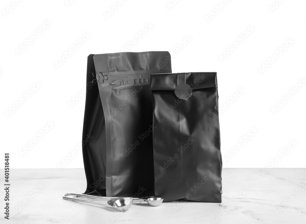 Bags with coffee and spoons on table against white background