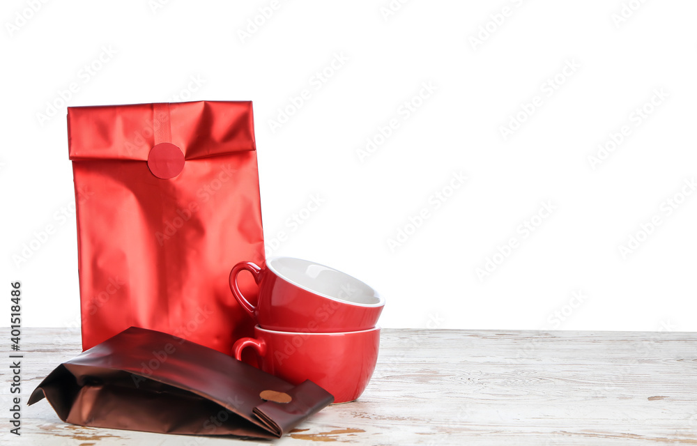 Bags with coffee and cups on table against white background