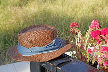 Straw hat on a summer's day rests on railings next to flowers with a blurred background of long grass in sunlight