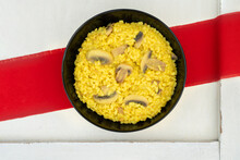Risotto With Saffron And Mushrooms In A Black Plate With A Red Line Napkin, Tablecloth On A White Background. Old Vintage Tray. 