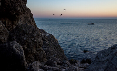 Rocky coast and a pleasure boat with tourists in the sea on a warm summer evening