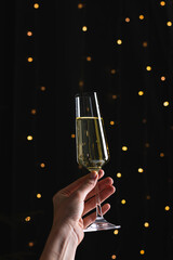 Wall Mural - Champagne in woman's hand on a black background with bokeh