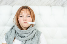 Sad Sick Young Girl Holds Thermometer In Her Mouth At Home. Empty Space For Text