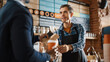 © Gorodenkoff - Handsome Barista in Blue Checkered Shirt Passes Coffe and Paper Bag with Pastry to an African American Customer. Concept of Buying Food and Drink in Modern Stylish Cafe.