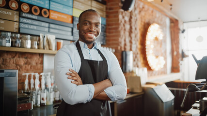 Handsome Black African American Barista with Short Hair and Beard Wearing Apron is Smiling in Coffee Shop Restaurant. Portrait of Happy Employee Behind Cozy Loft-Style Cafe Counter.