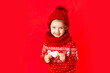 © Any Grant - a little girl in winter clothes holds a heart on a red background. New year's or Valentine's day concept, place for text